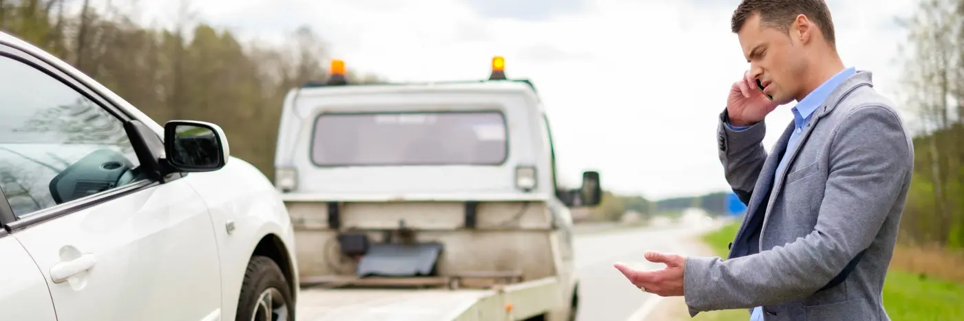 Mand i habitjakke taler i mobiltelefon ved havareret bil
